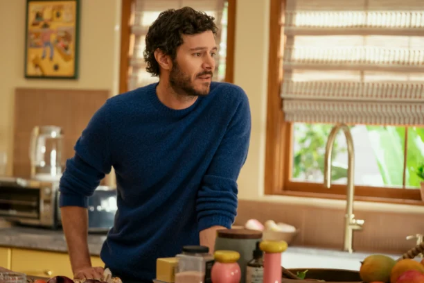 NWT 305 Unit 00436RC2X2.jpg "A man with curly hair and a beard wearing a blue sweater stands in a cozy kitchen leaning on the counter, surrounded by cooking ingredients, with sunlight coming through the window blinds."